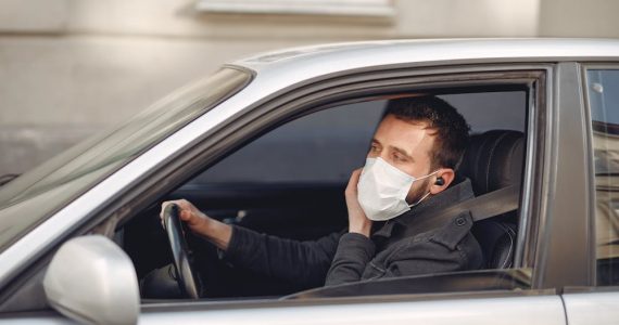 Is it illegal to drive with headphones - man wearing a mask speaking by true wireless earphones driving car on urban street.